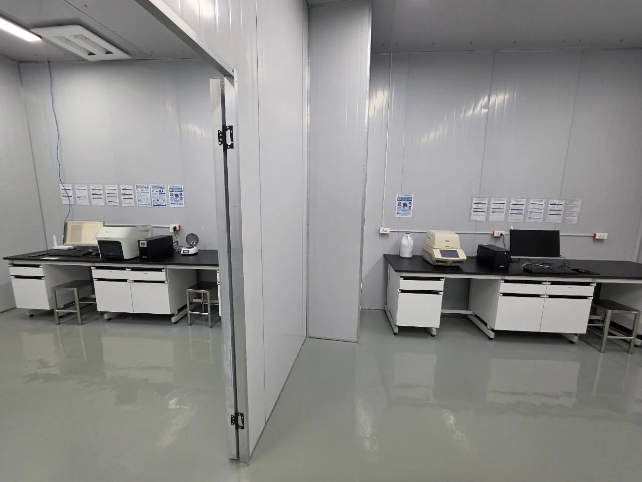 Two adjoining laboratory rooms with a dividing wall and equipment on their workbenches